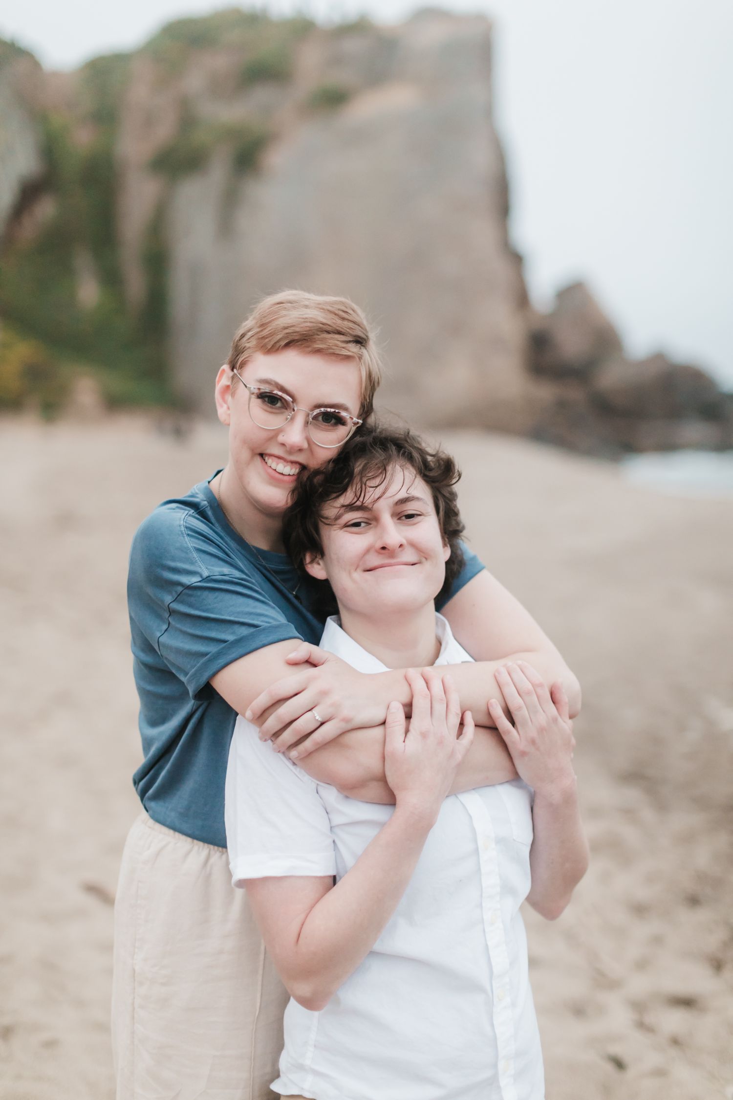 Loving embrace of two people on a beach with rocky cliffs in the background.