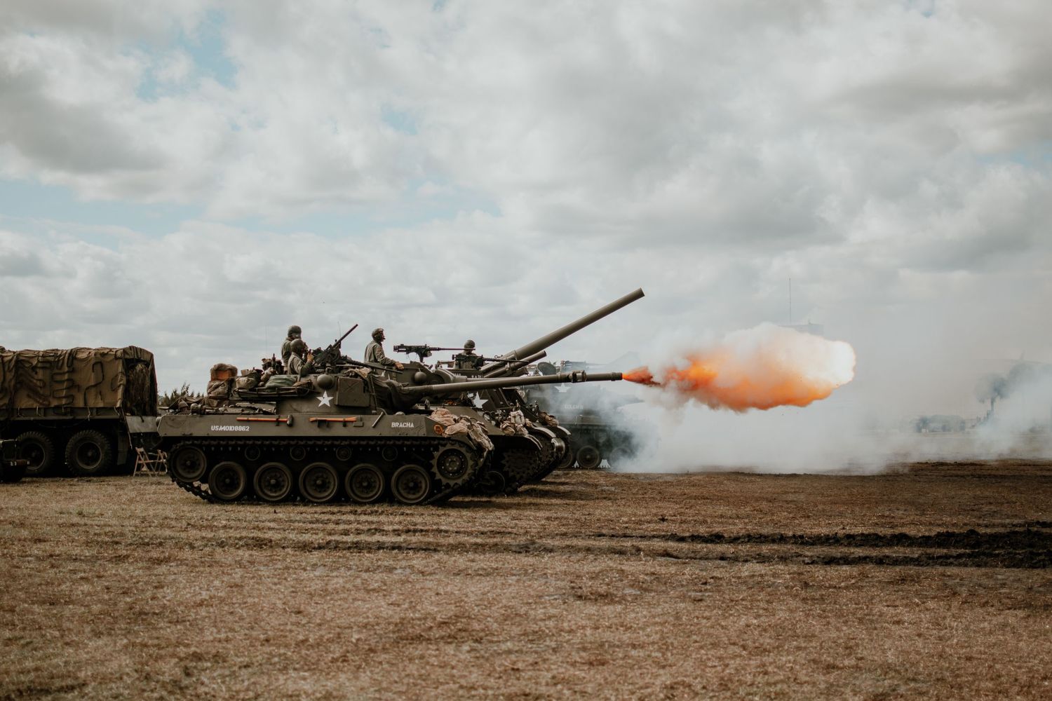 Military tanks firing on a battlefield with smoke and explosions visible.