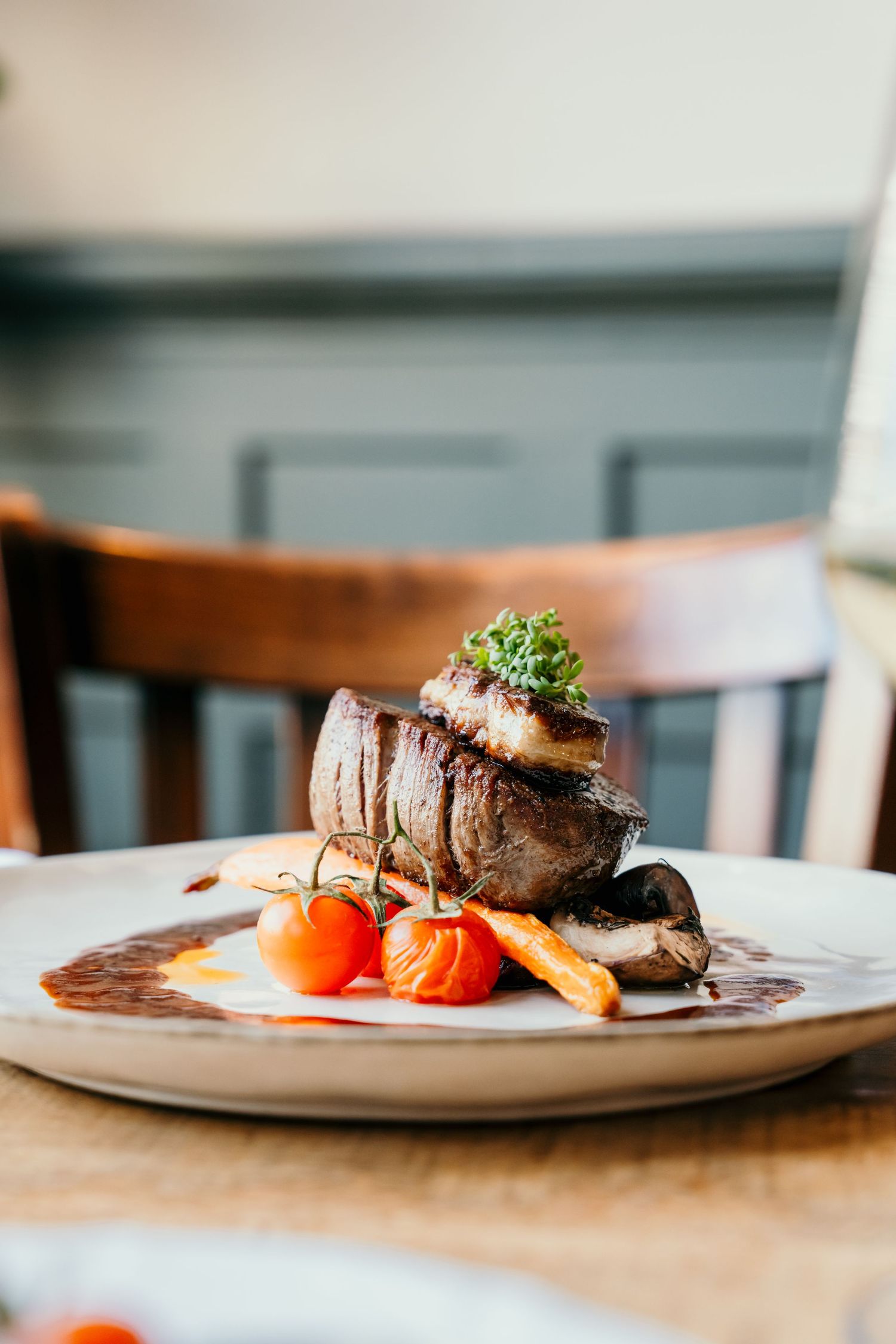 Perfectly plated filet mignon with roasted vegetables and garnish on a white plate.