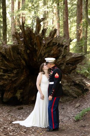 Marine groom kissing bride before giant redwood tree roots.