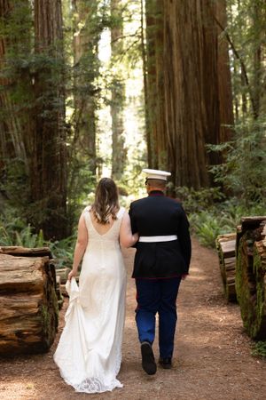 Marine groom and bride walking arm in arm through redwood forest.