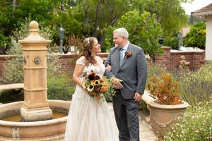Bride and groom smiling together near stone fountain in a beautiful garden setting.