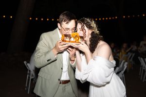 Bride and groom sharing a joyful bite of wedding cake together under string lights at outdoor night reception.
