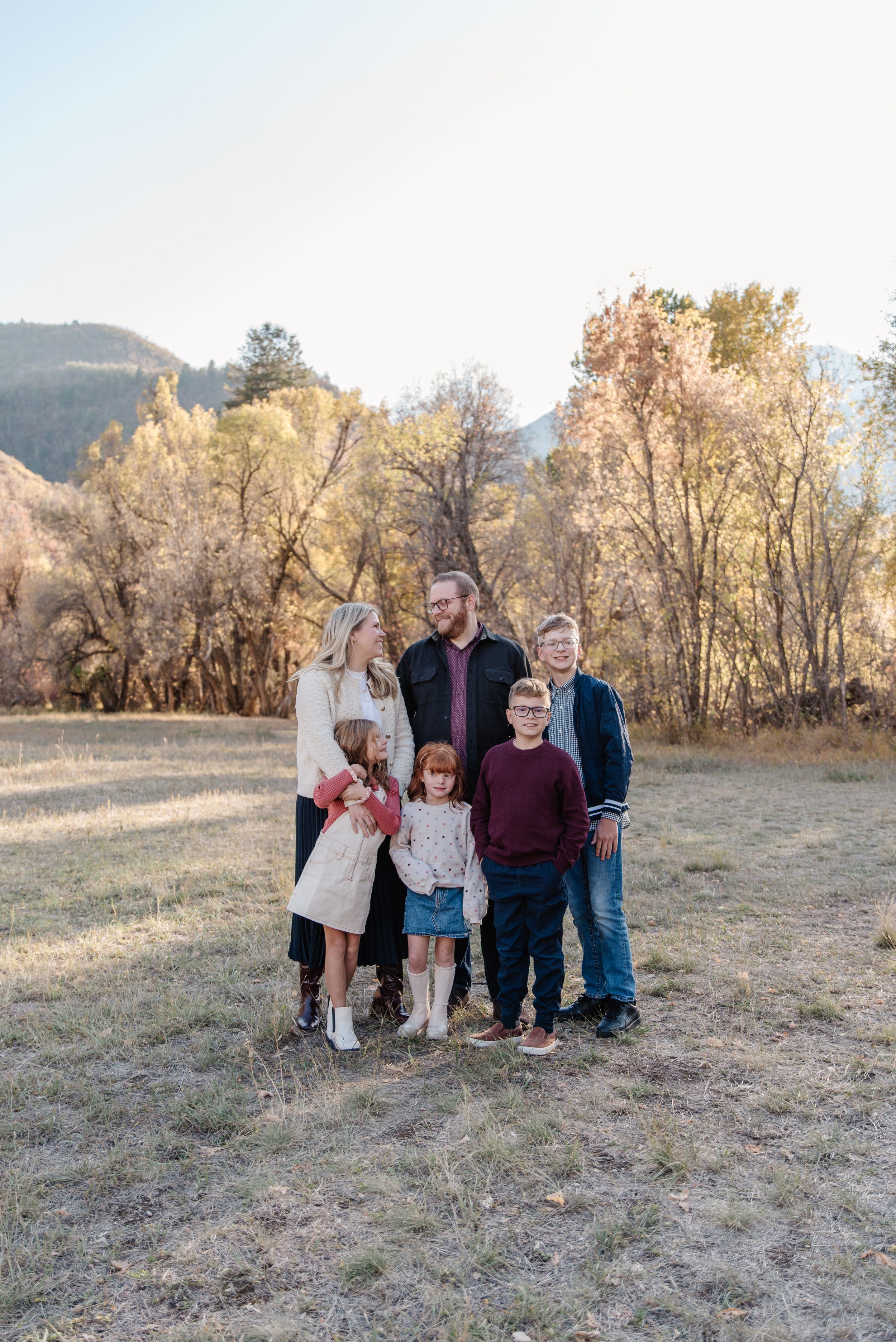 Family portrait taken outdoors in autumn with mountains and trees in background.