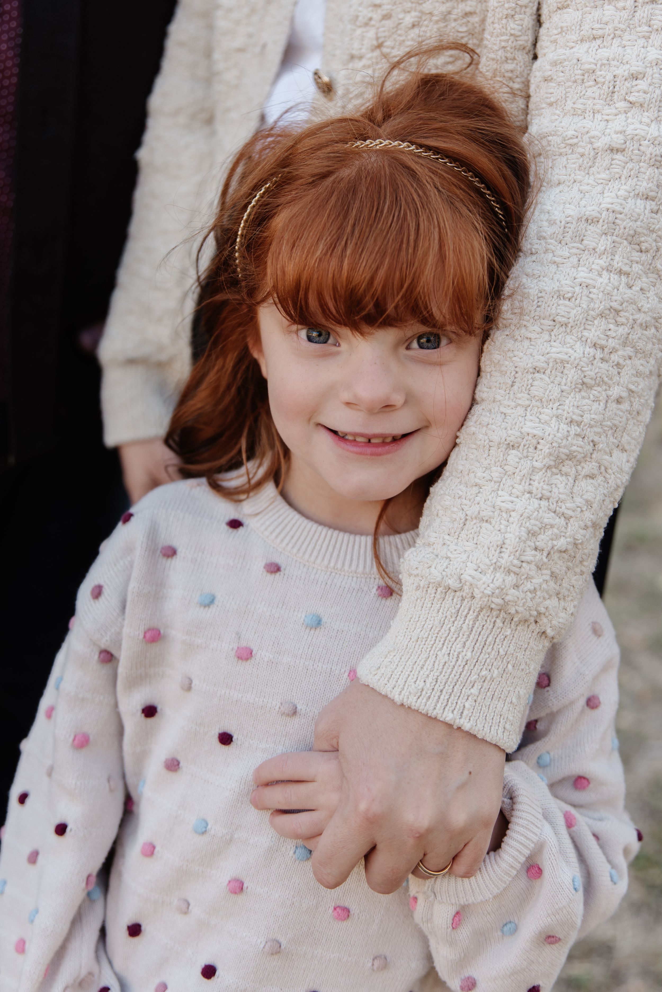 Young child in polka dot sweater smiling while holding adult's hand.
