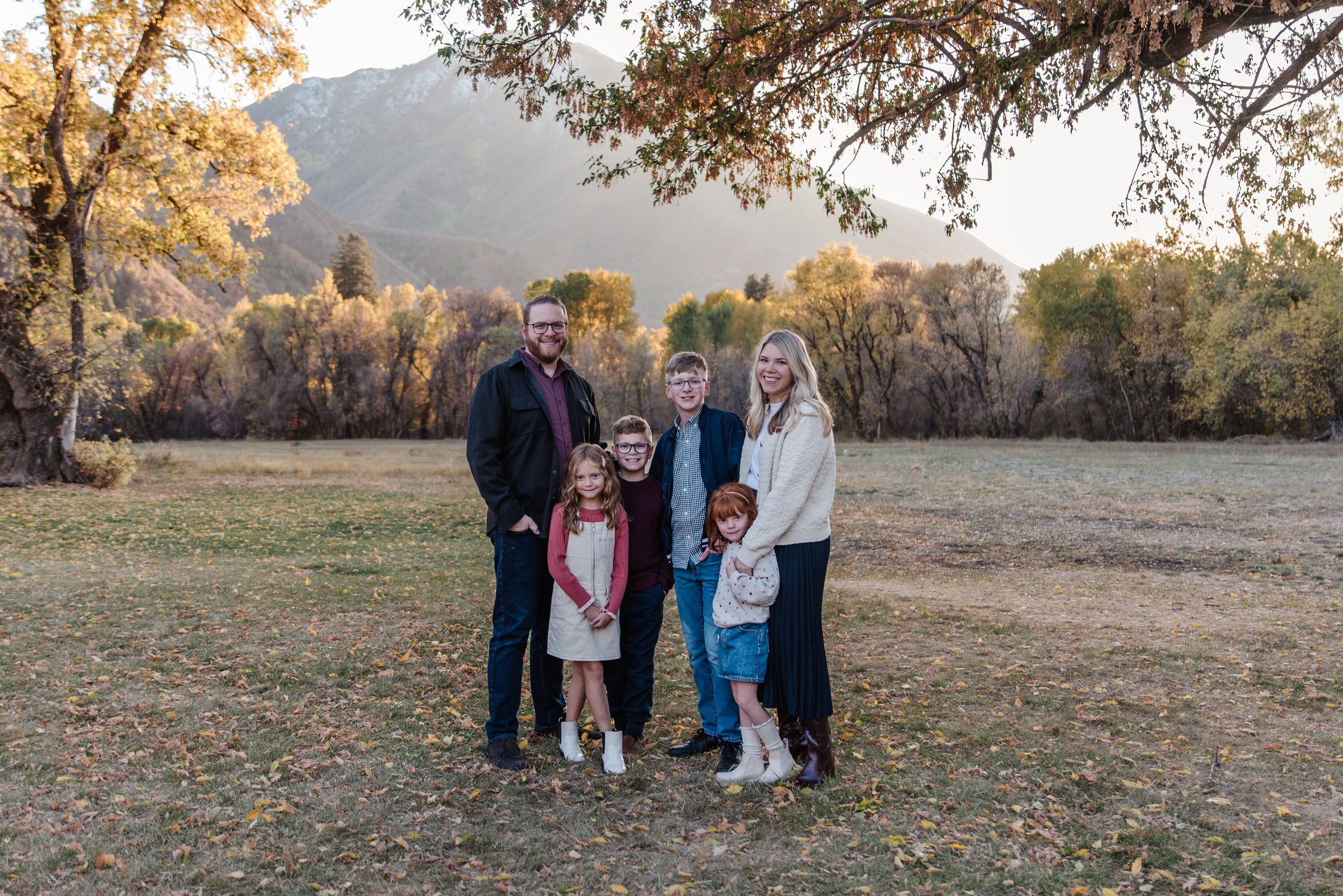 A family poses together in a fall setting with golden trees and mountains in the background.