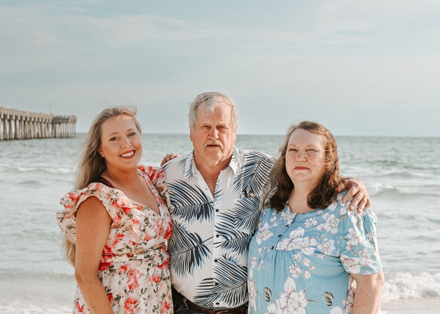 Group wearing coordinated tropical outfits smiles together on sunny beach.