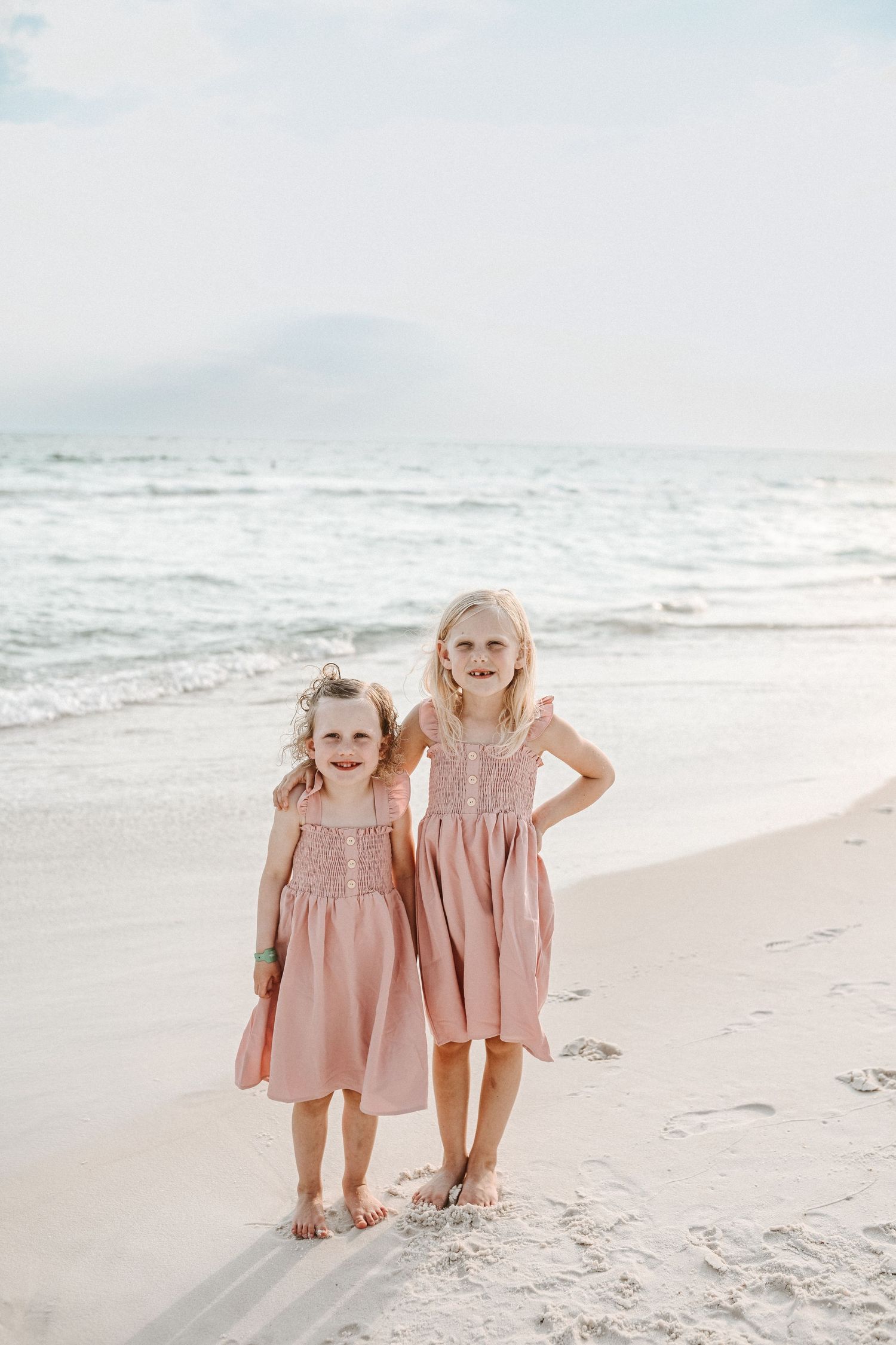 Two children in matching pink dresses play on white sandy beach.