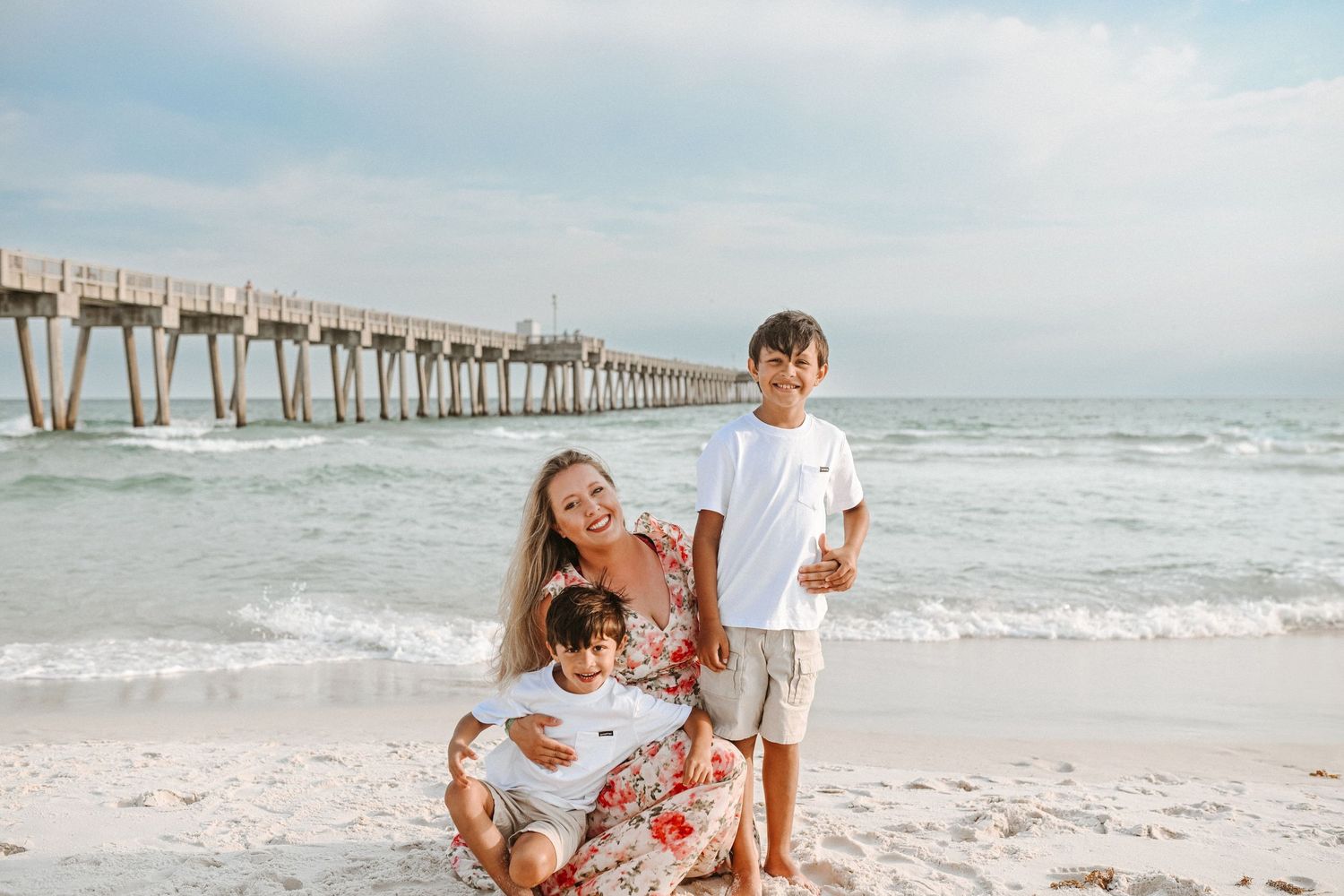 Beach family photoshoot with wooden pier and ocean waves in background.