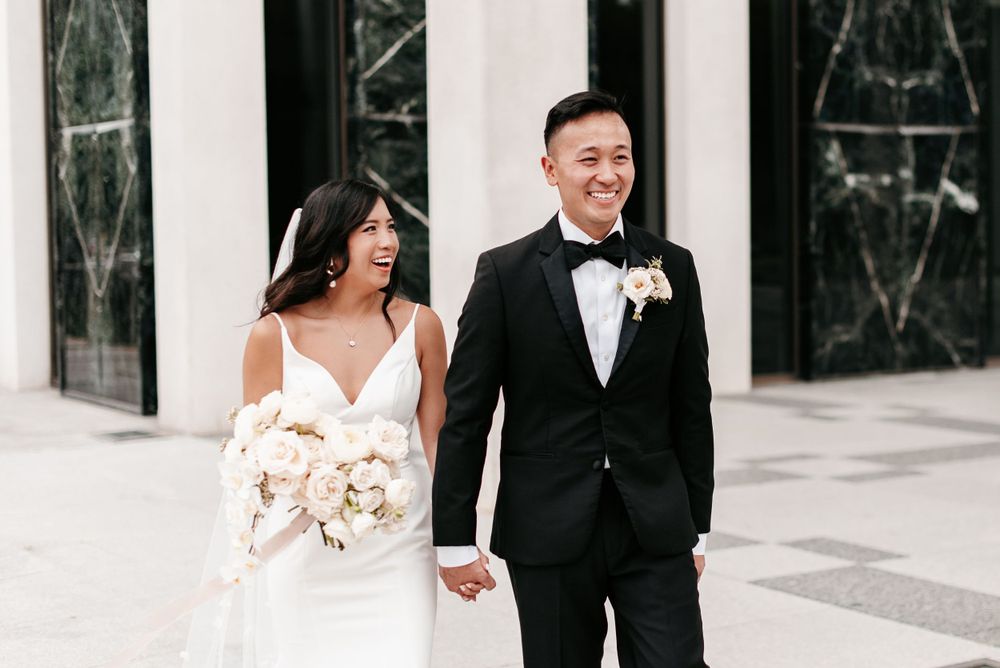A bride and groom holding hands and laughing while walking outside of the ING Building in Minneapolis, Minnesota. Lindsay Miller Photograph