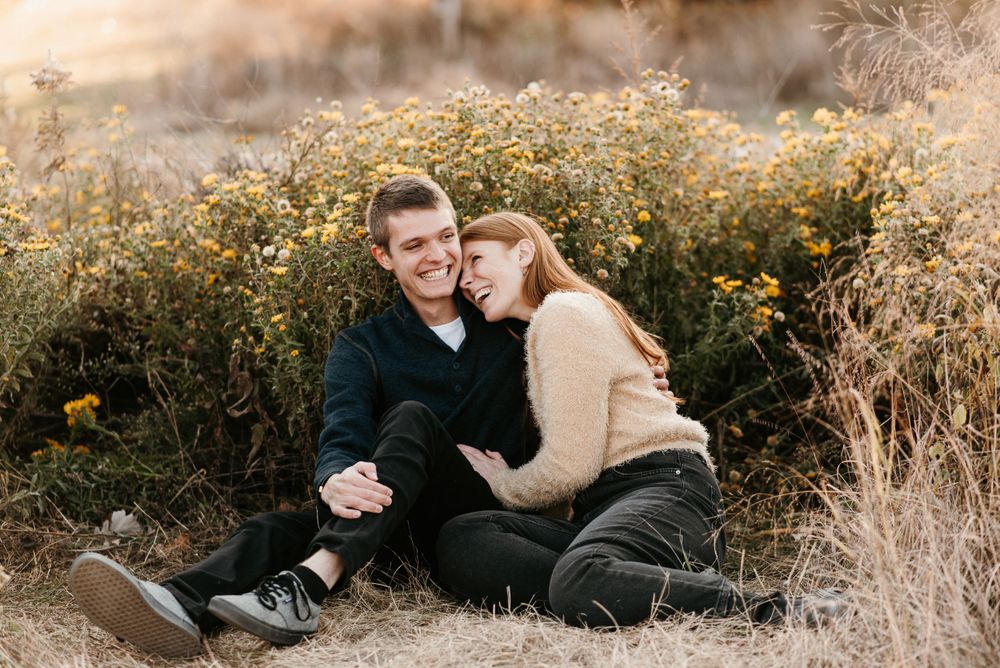 A couple cuddling and laughing in front of wildflowers at Schaar’s Bluff Gathering Center in Hastings, Minnesota. Lindsay Miller Photography