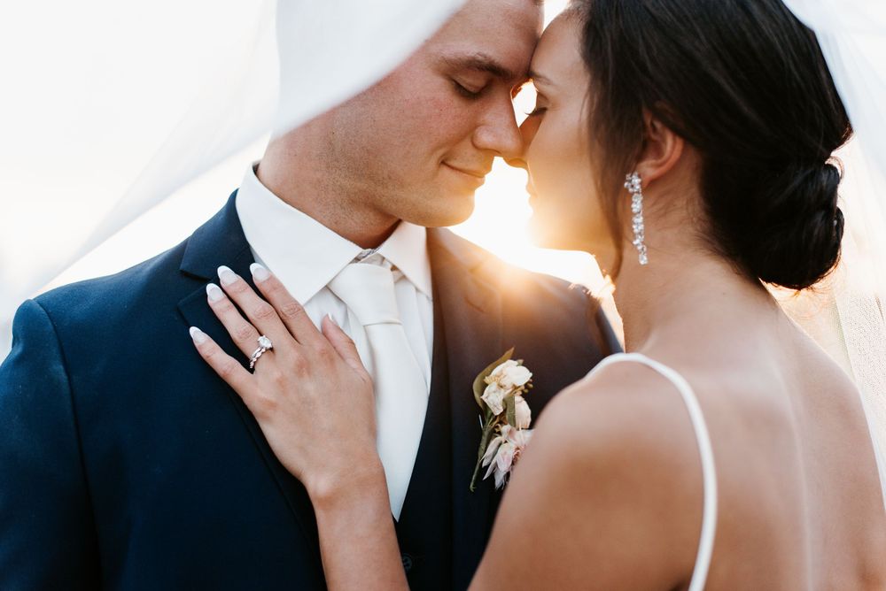 A bride and groom embracing, with the sun peeking through their faces at 45th Parallel in Wisconsin. Lindsay Miller Photography