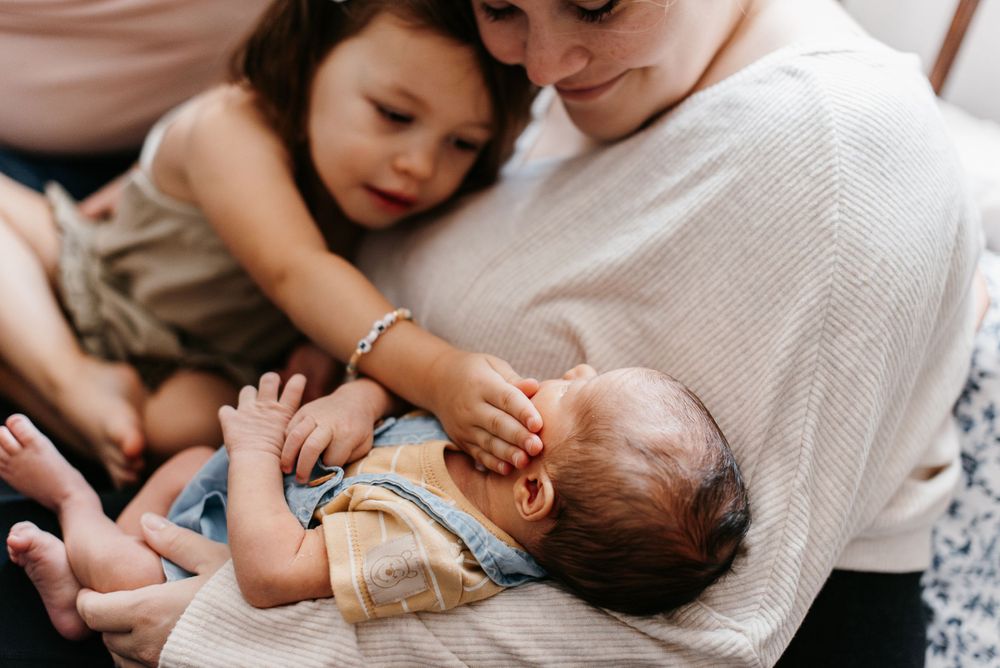 A mother holding her newborn son, while her daughter caresses the baby's cheek. Lindsay Miller Photography
