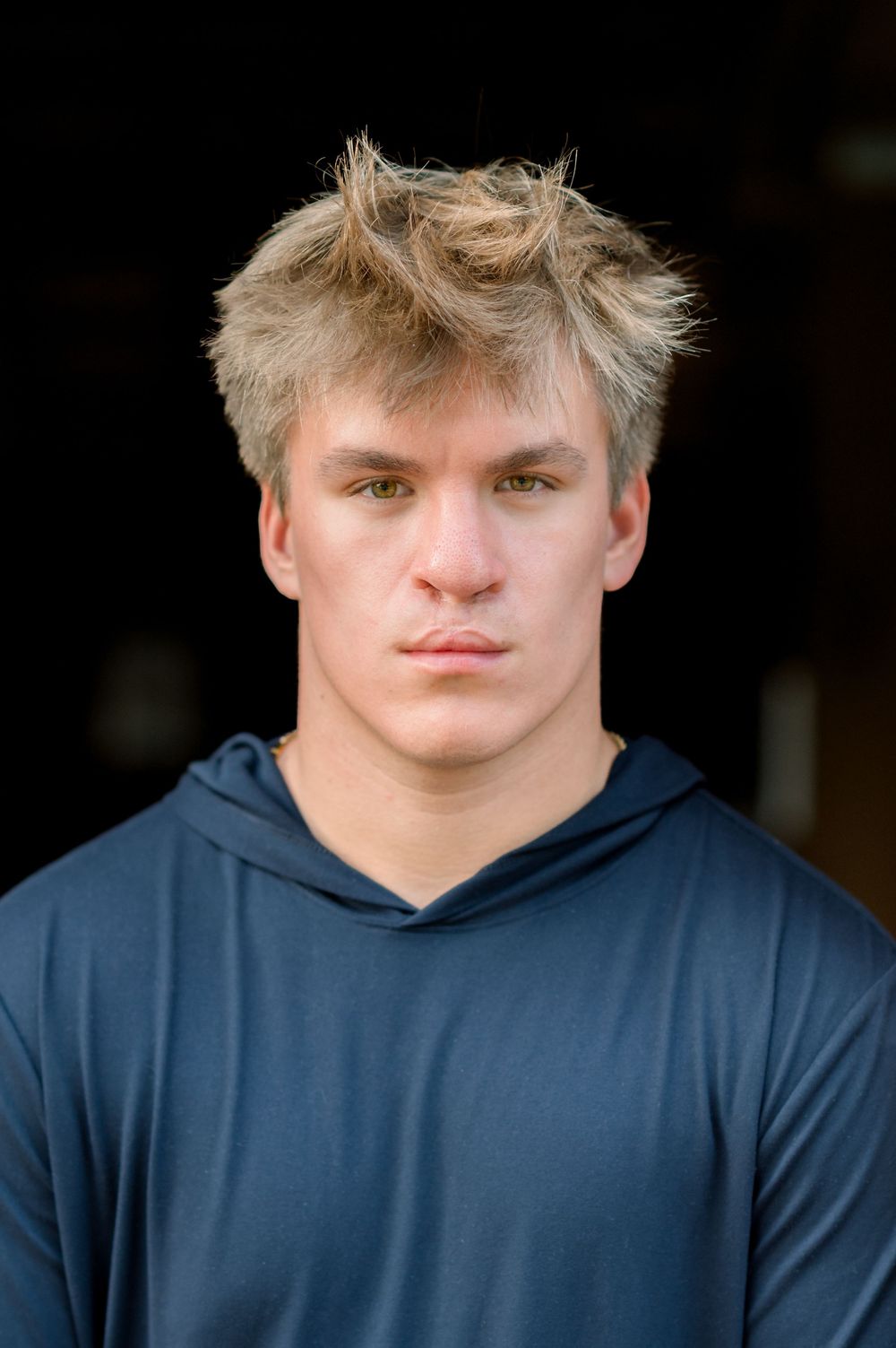 Person wearing a navy blue hoodie poses against dark background with blonde spiky hair.