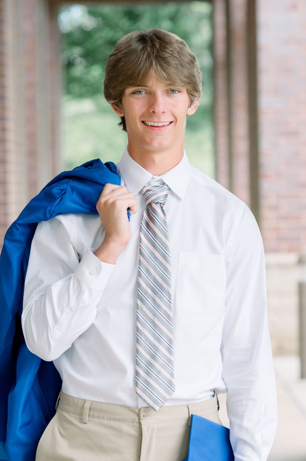 Young student in professional attire with a white dress shirt, striped tie and blue jacket draped over shoulder on campus.
