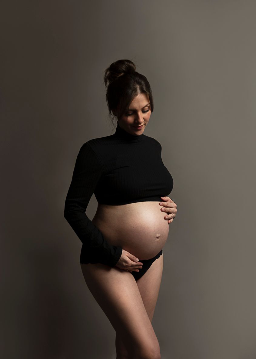 Artistic maternity photo featuring a black bodysuit against minimalist grey backdrop.