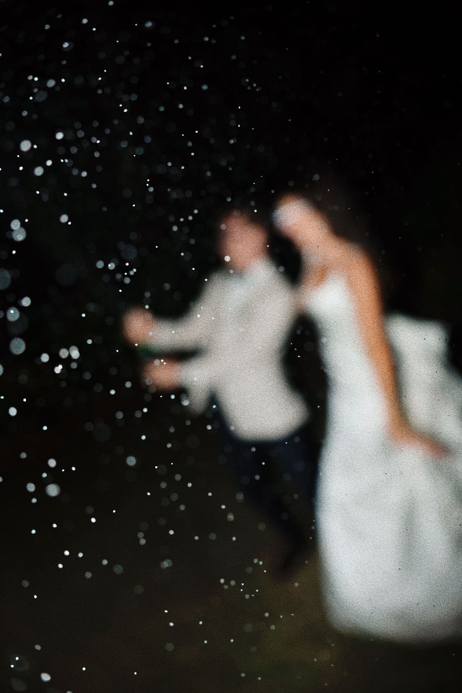 Blurred silhouettes dancing with falling snow or sparkles against dark background.