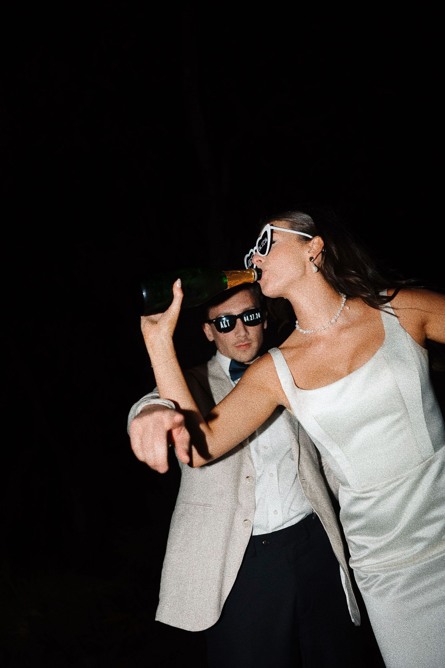 Two people dancing and posing together in black and white clothing against a dark background.