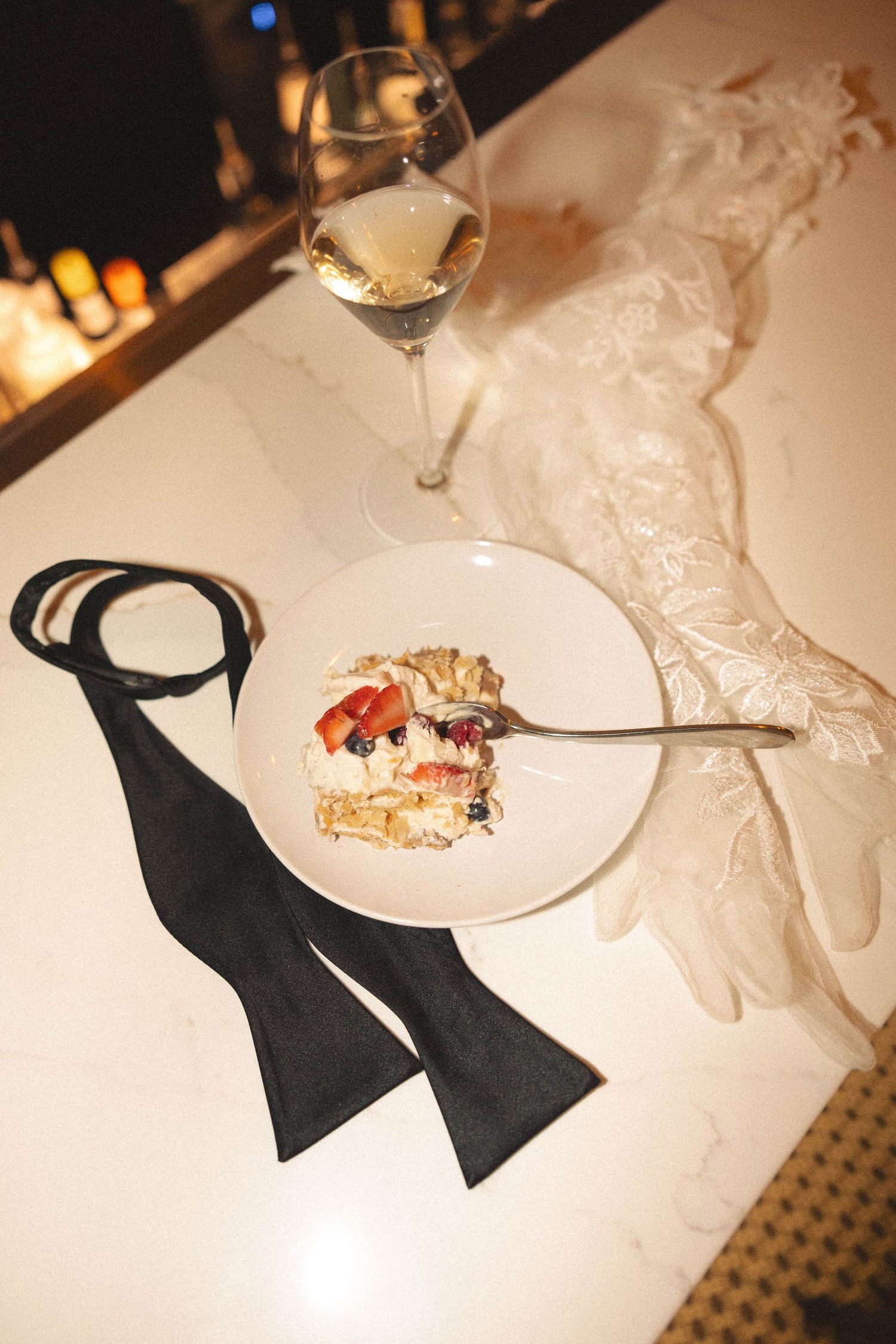 Elegant place settings with black bow ties and white plates on a formal dining table in warm lighting.
