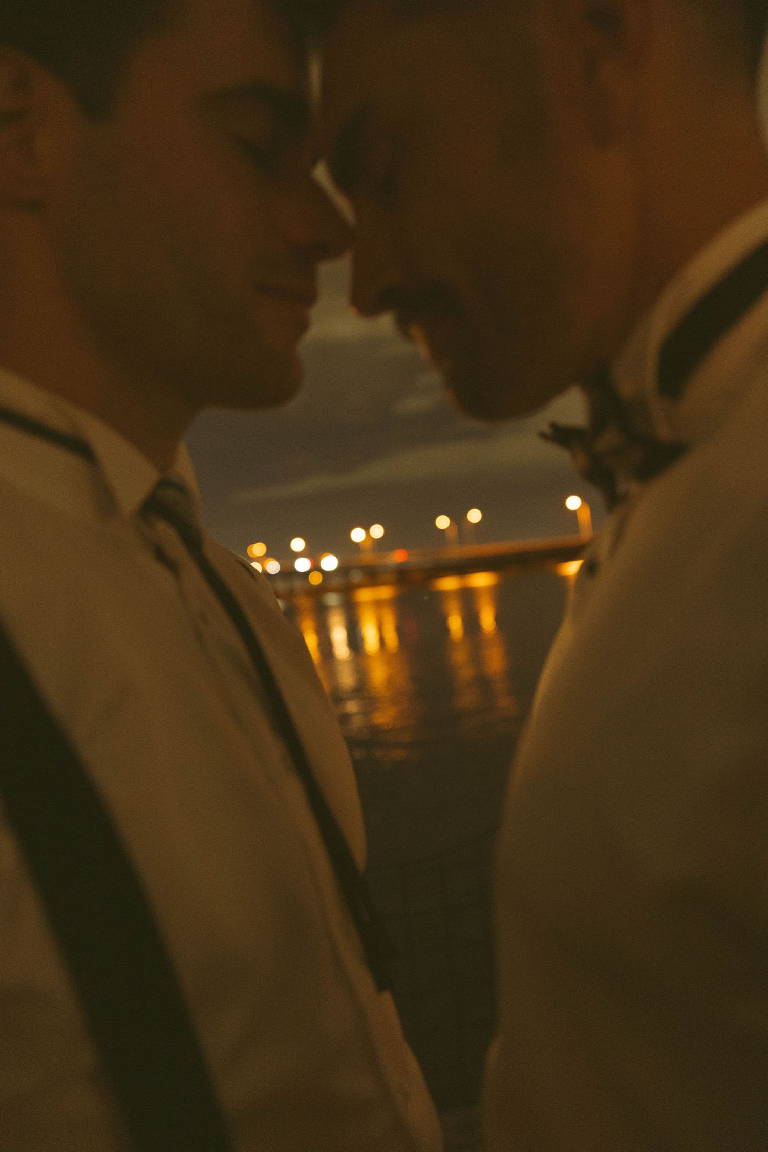 A silhouetted couple in formal attire stands close together against a warm glowing background with bokeh lights.