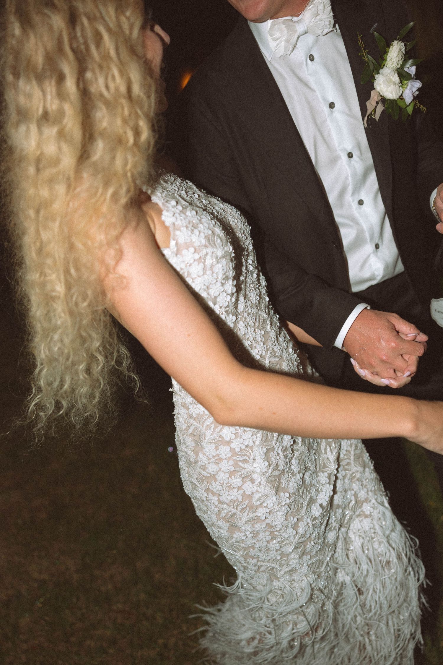 A couple dances at a wedding reception, with the bride wearing a textured white lace gown and the groom in a dark tuxedo.