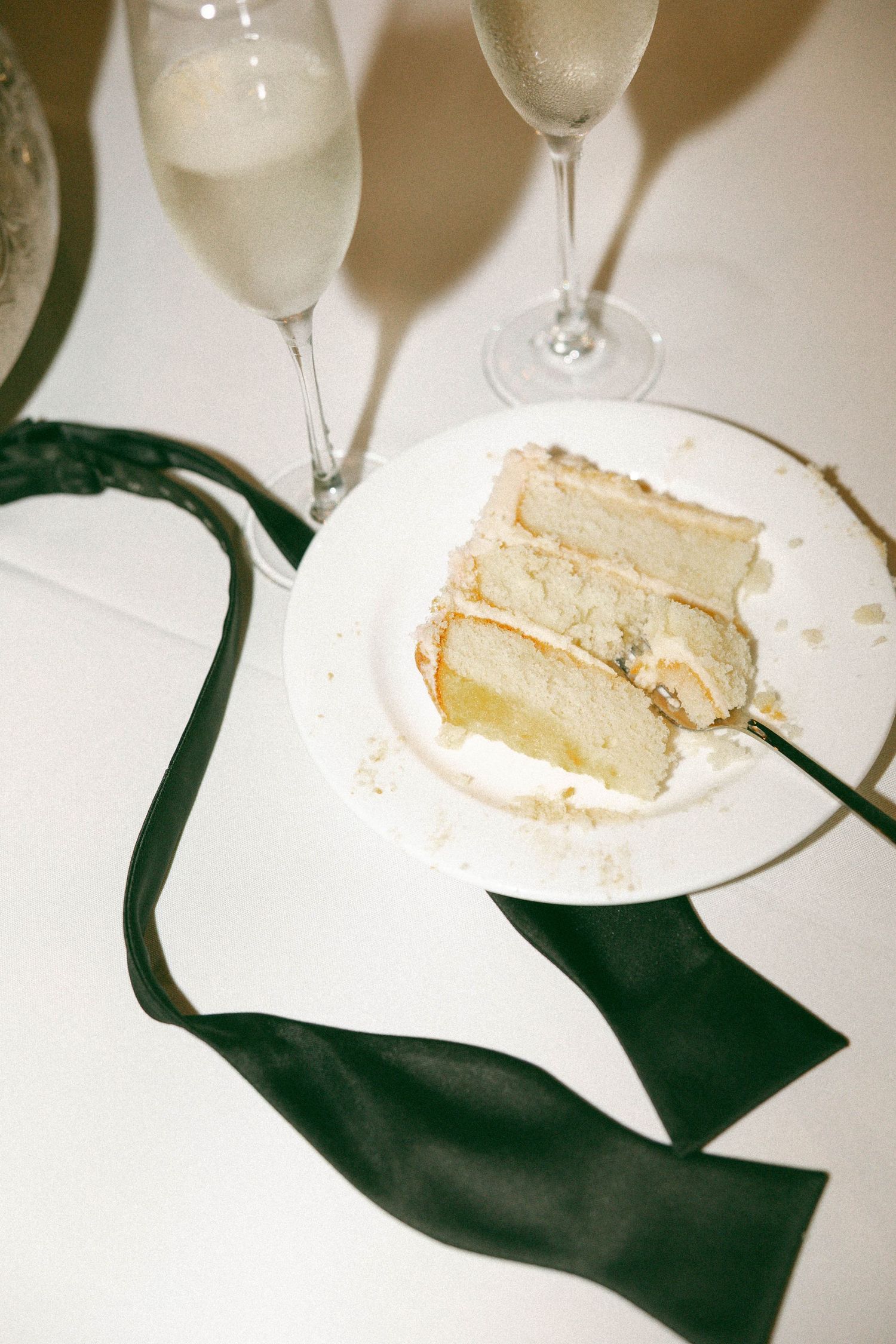 A series of white plates showing a slice of vanilla cake being eaten progressively smaller with wine glasses visible.
