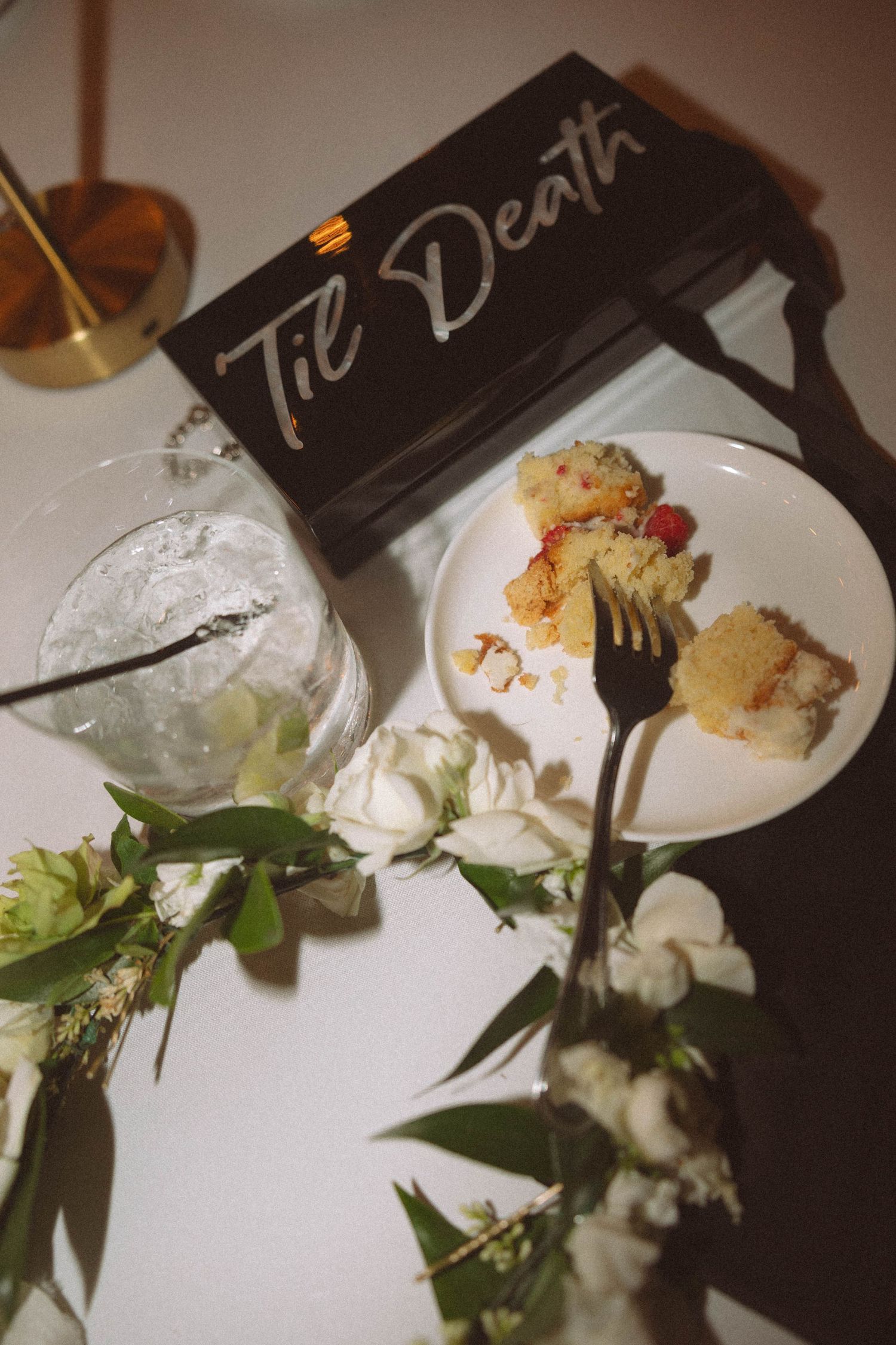 Elegant plated dessert with white cream and garnishes on dark table setting with decorative flowers.