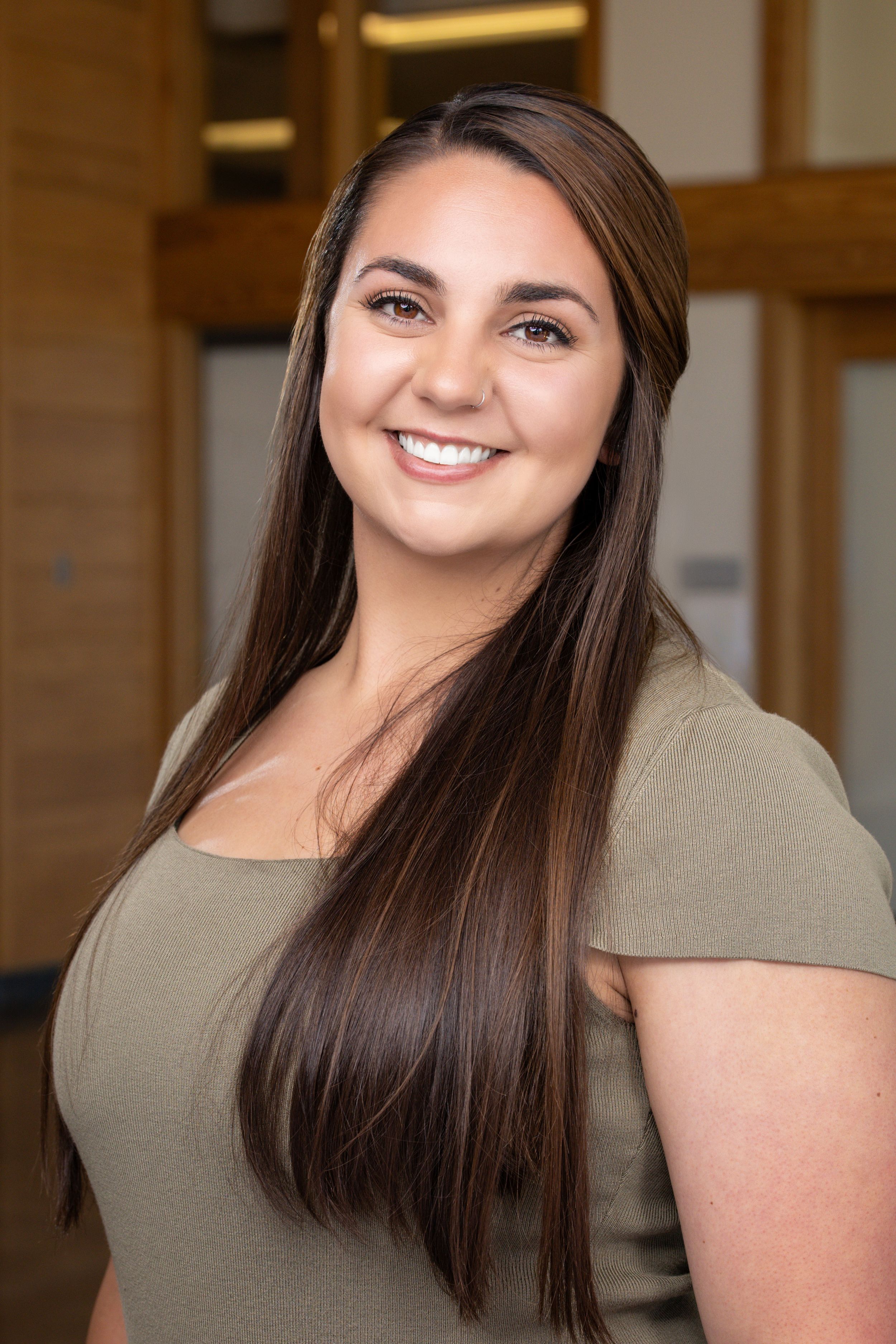 Smiling young woman with long dark hair wearing an olive green top in a professional headshot photo.