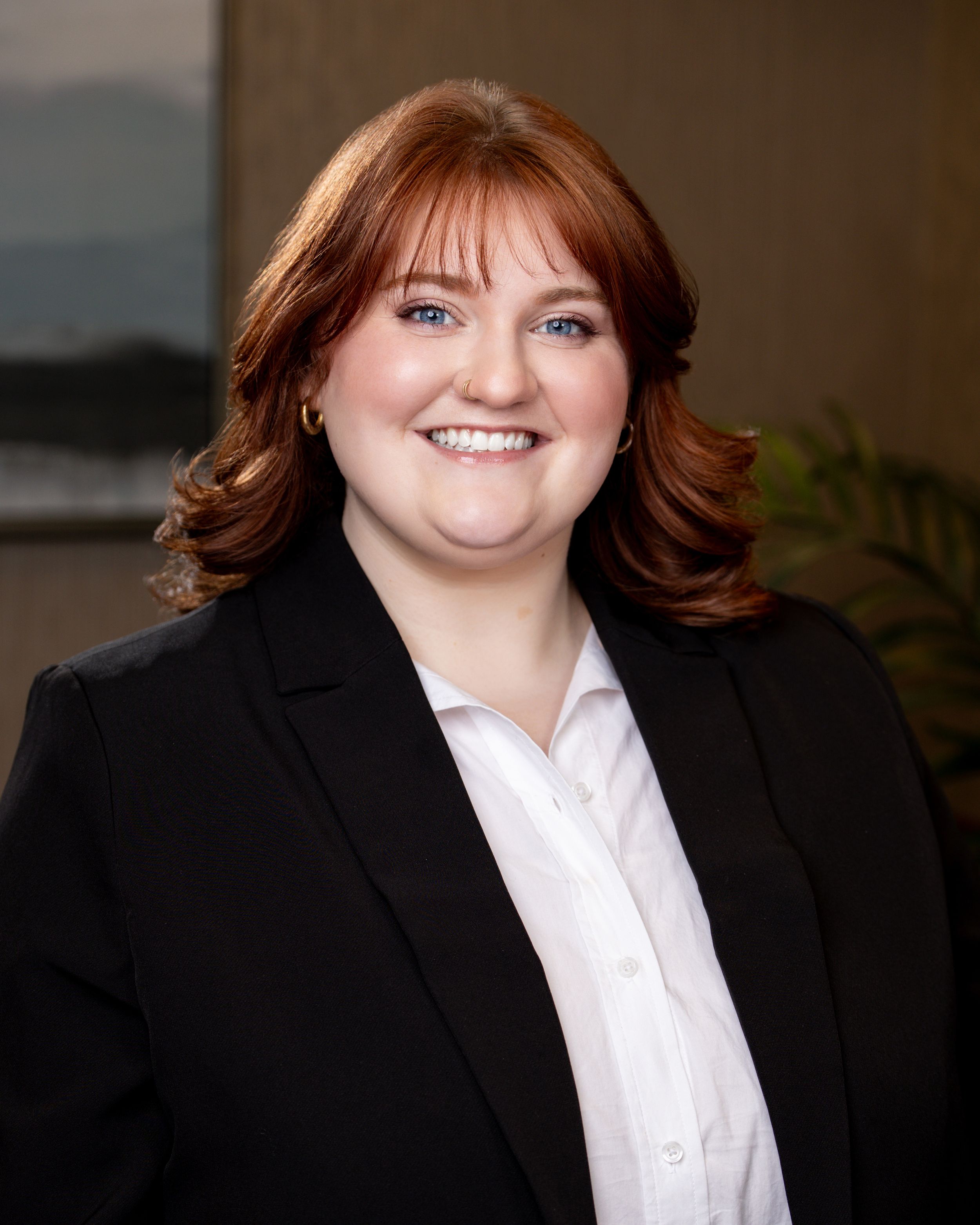 Professional headshot of a smiling woman with red hair wearing a black blazer and white shirt.