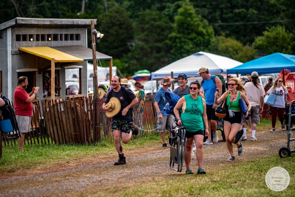 People running and walking at an outdoor festival with colorful tents and wooden fences on a cloudy day.