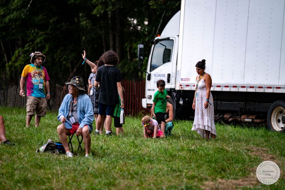 Group of people gathered on grass near a large white truck at an outdoor festival event.