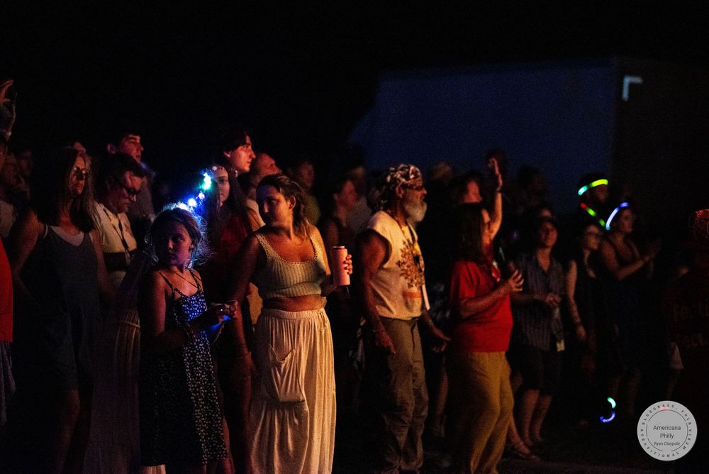 Crowd of people enjoying an outdoor night concert with colorful glow sticks and raised hands.