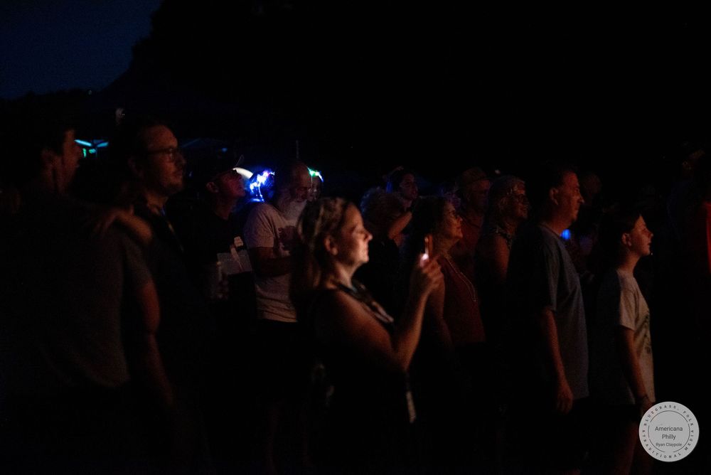 Crowd of people watching an outdoor nighttime event with glowing blue lights in the dark.