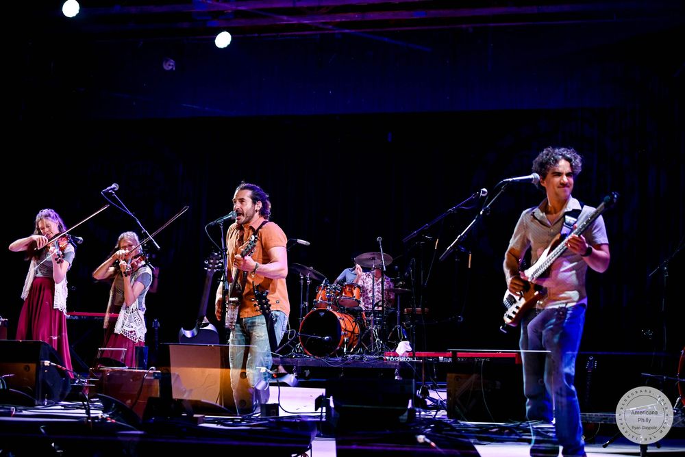 Live band performing on stage with guitars and violins under blue and red stage lights.