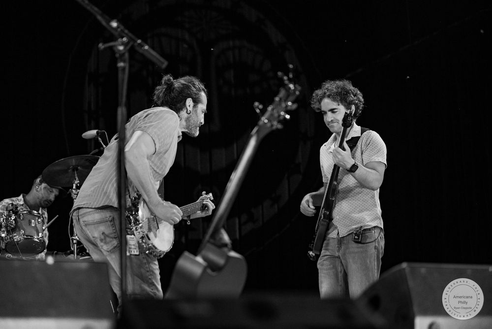 Two male musicians playing guitars on stage in black and white concert photography.