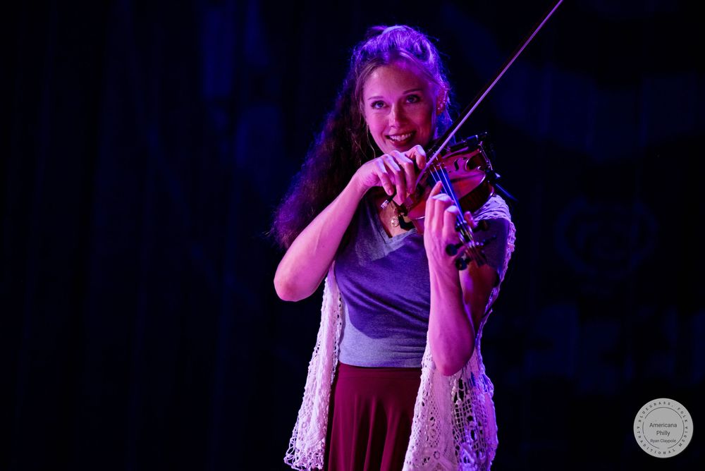 Young woman playing violin on stage under purple stage lighting during a live performance.