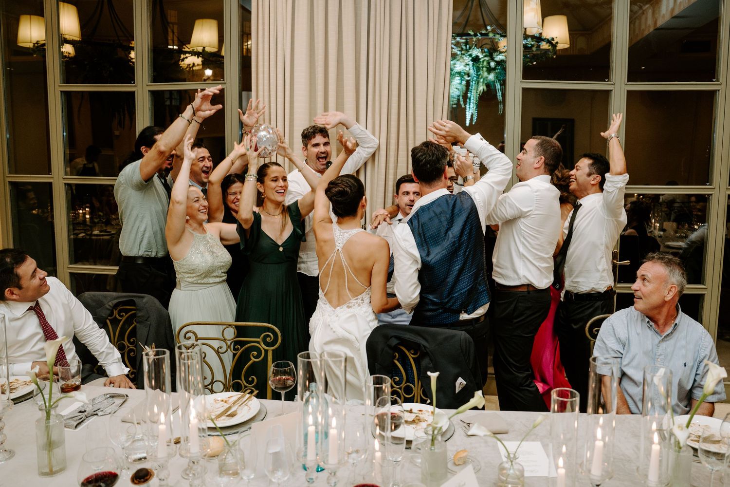Wedding guests celebrate with raised hands and sparklers at an elegant indoor reception dinner.