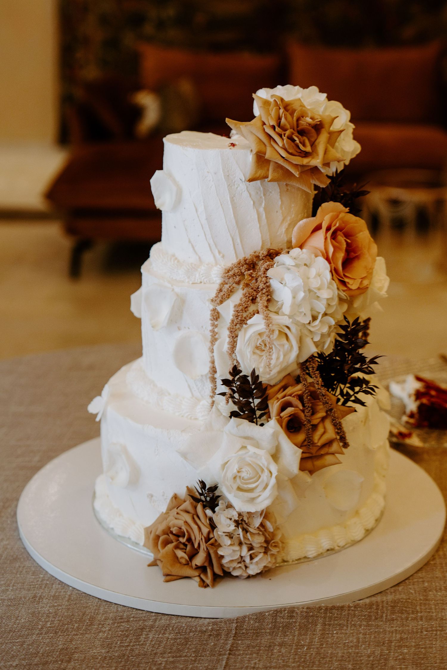 Elegant three-tier white wedding cake adorned with gold and white roses and floral decorations.