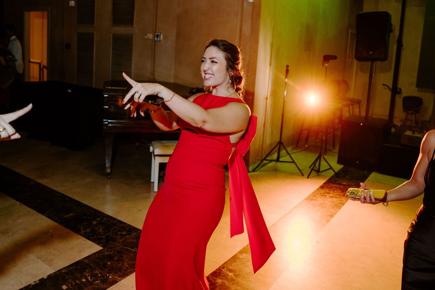 Woman in red gown dancing joyfully at elegant wedding reception venue.