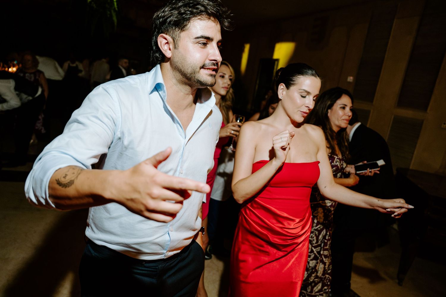 Couple dancing energetically at a party, man in white shirt and woman in red dress on a dance floor.