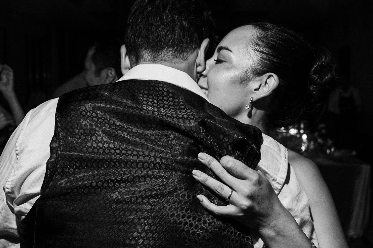 Black and white photo of a couple sharing a romantic kiss at a wedding reception.