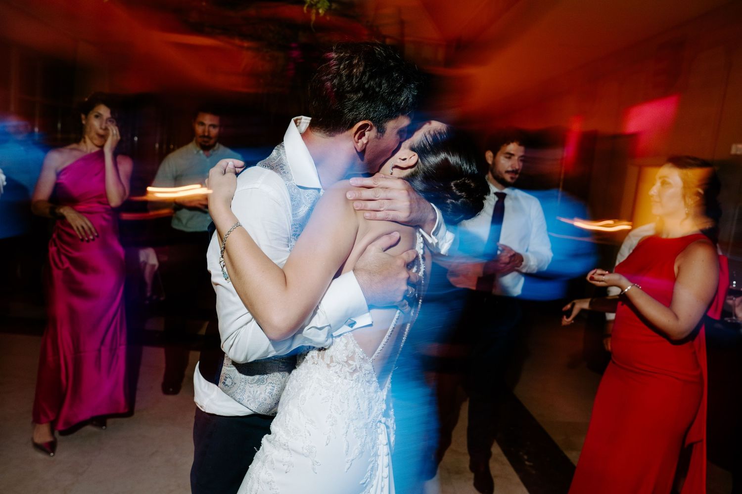 Couple sharing romantic embrace on dance floor surrounded by wedding guests.
