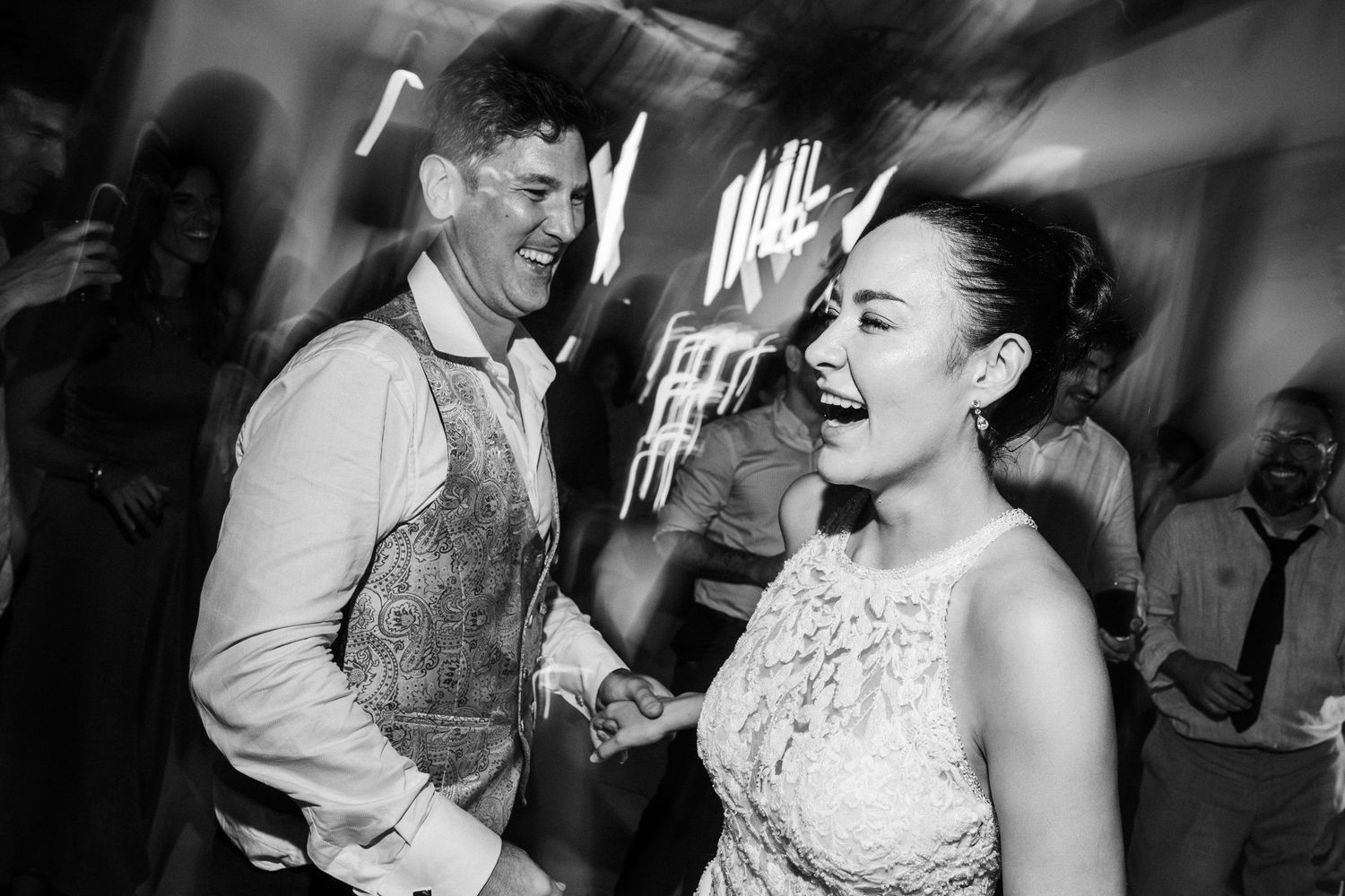 Black and white photo of a joyful couple laughing and dancing together at a lively celebration.