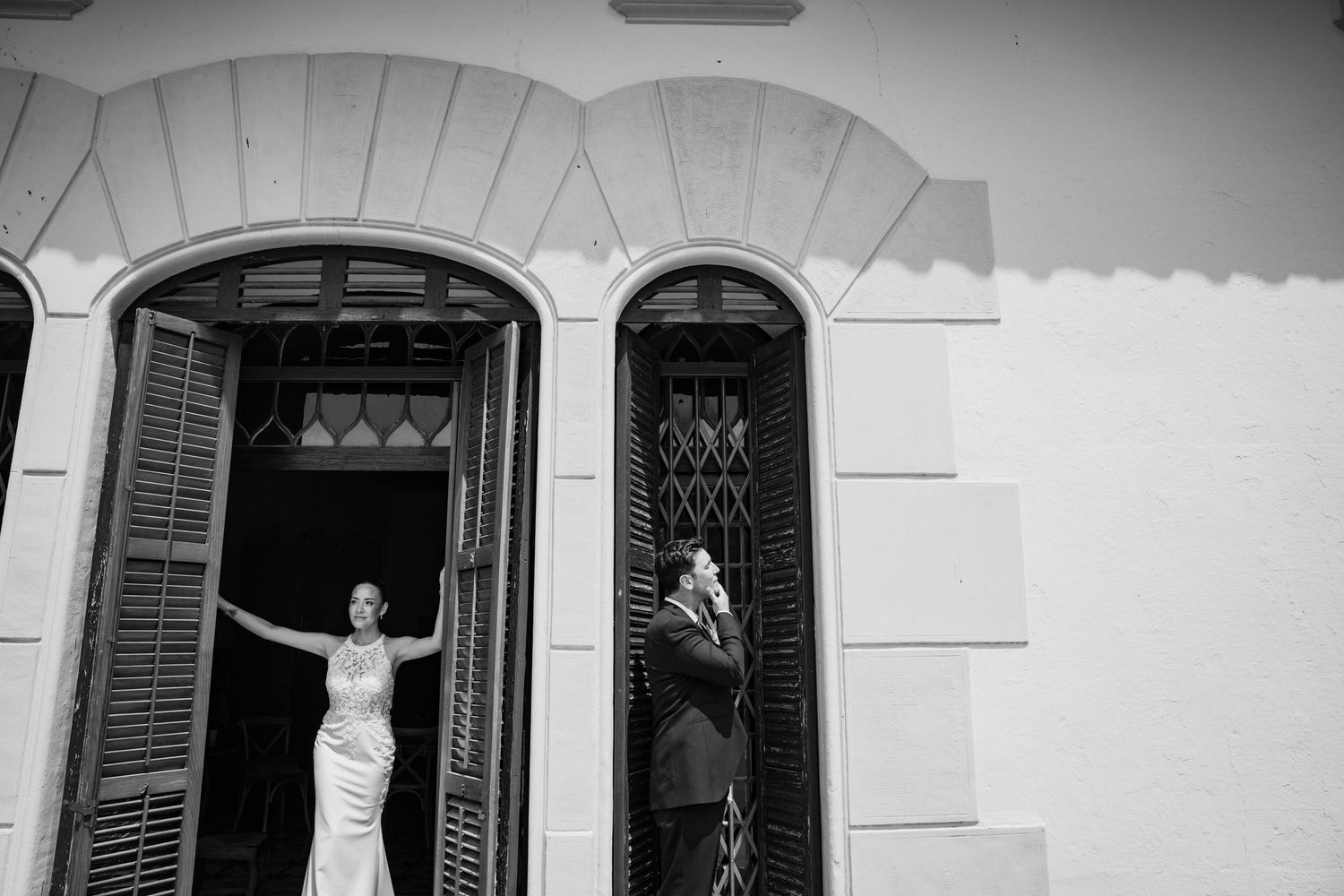 Black and white photo of bride and groom at arched windows of elegant building on wedding day.