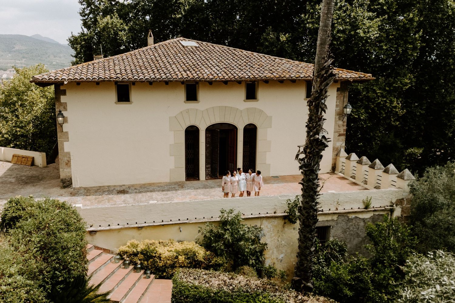 Wedding party poses on terrace of a charming Italian-style villa surrounded by lush greenery and gardens.