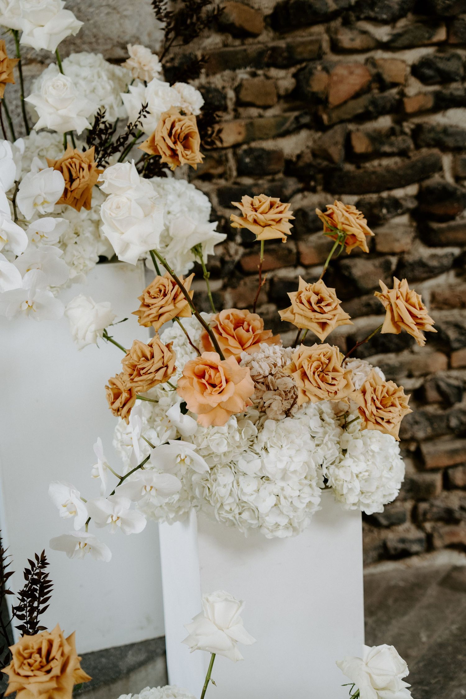 Elegant wedding floral arrangement with peach roses and white hydrangeas against rustic stone wall.