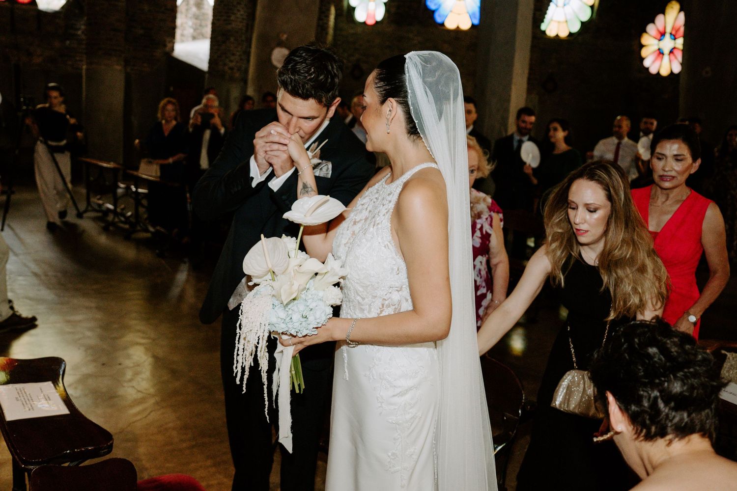Bride and groom share first kiss at church altar during wedding ceremony with guests watching.