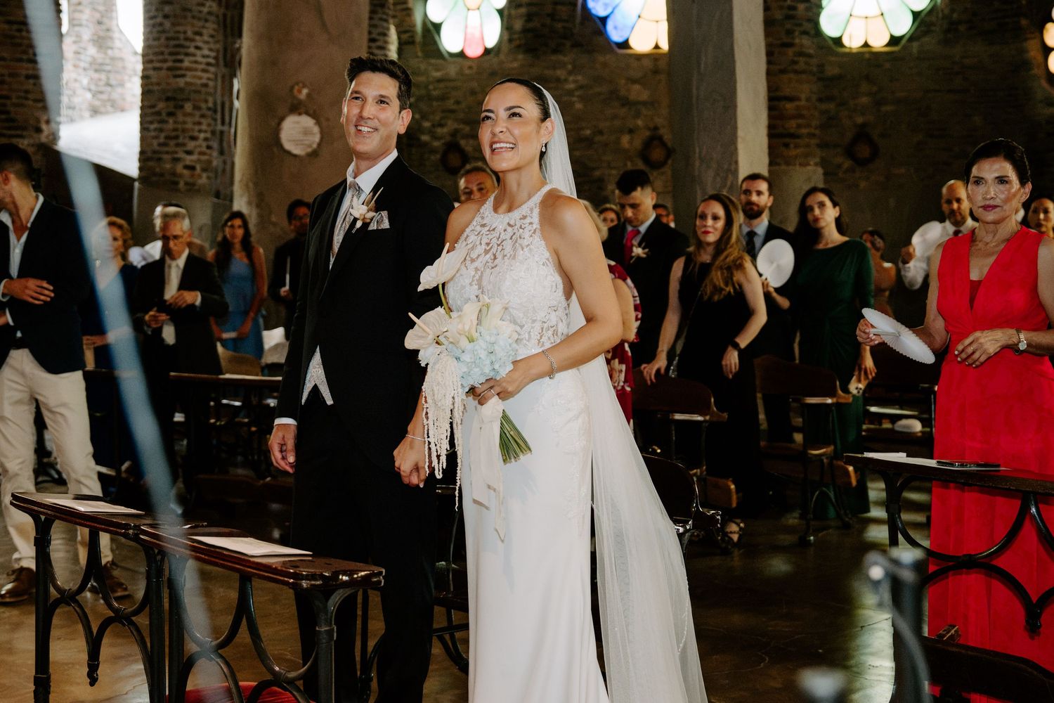 Smiling bride and groom walking down aisle in rustic stone church during wedding ceremony.