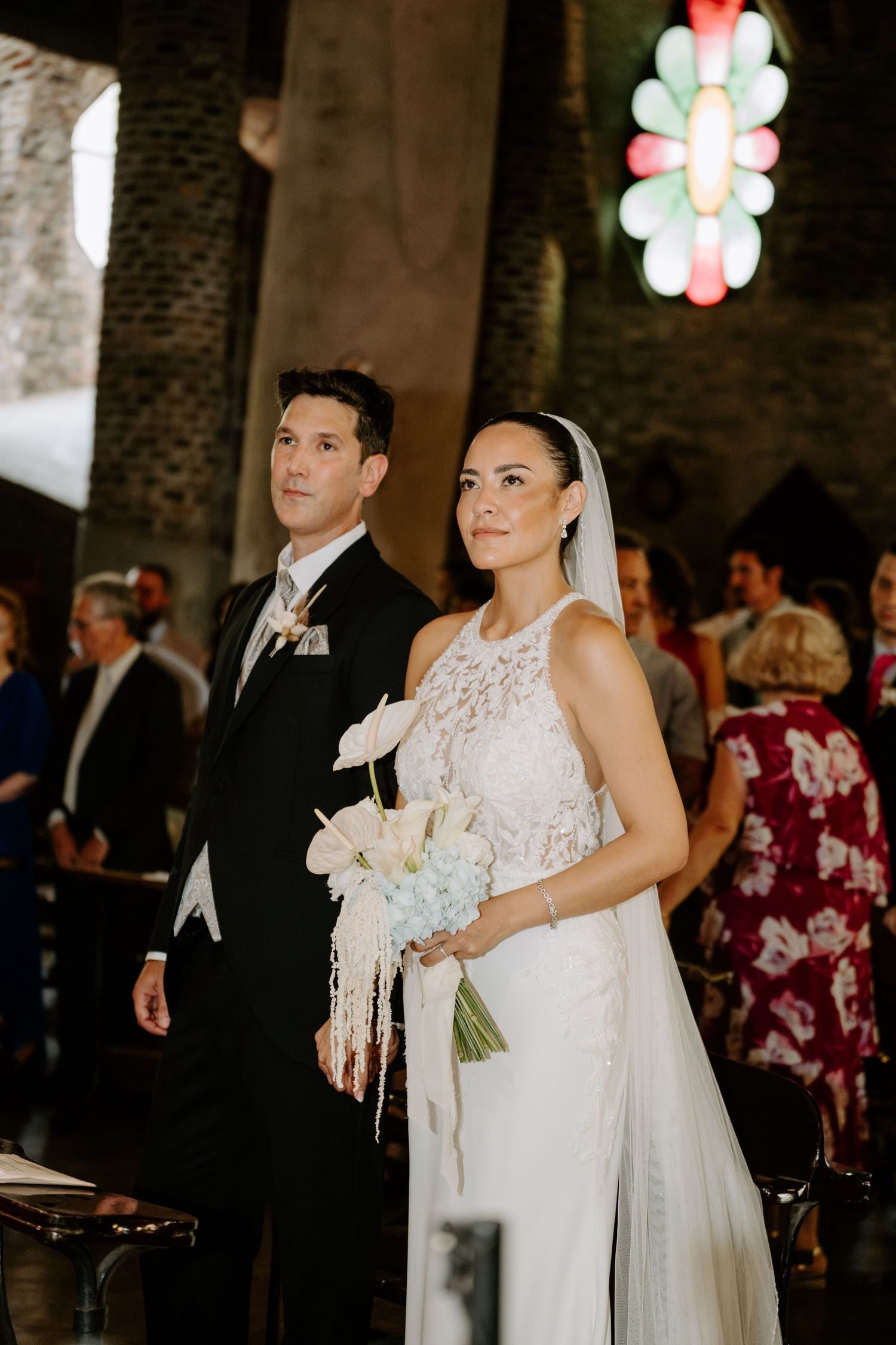 Bride and groom walking down the aisle in a church, bride holding white floral bouquet in elegant lace wedding gown.