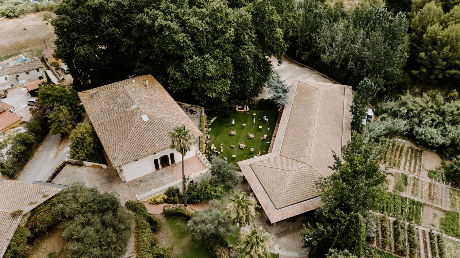 Aerial view of a rustic wedding venue surrounded by lush green trees and manicured gardens.